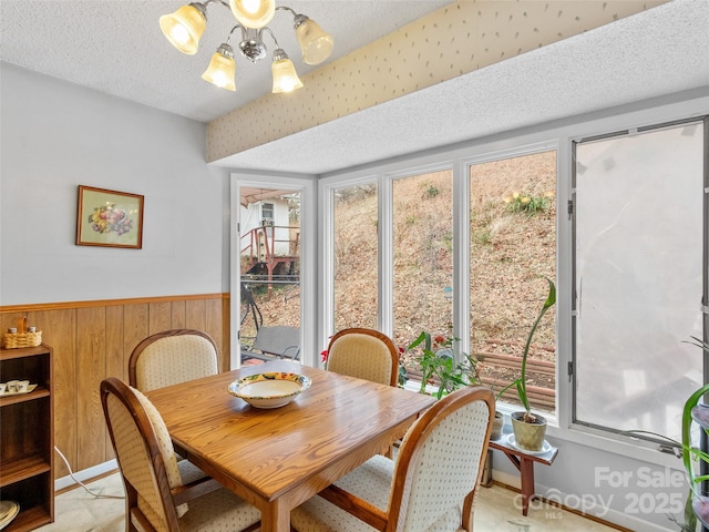 dining area featuring a wainscoted wall, wood walls, a textured ceiling, and an inviting chandelier