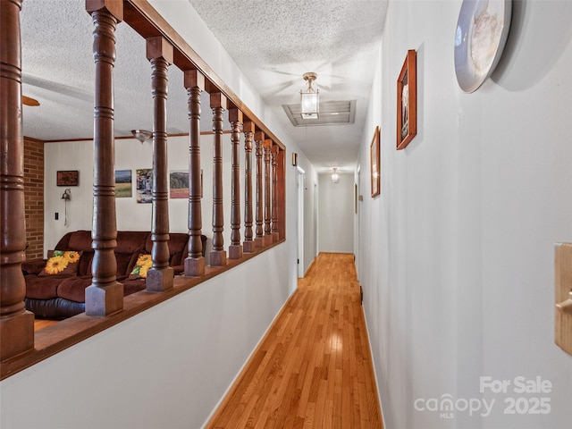 corridor with baseboards, a textured ceiling, and light wood-style floors