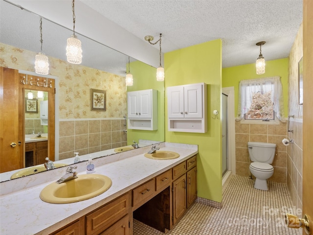 bathroom featuring wallpapered walls, a textured ceiling, tile walls, and a sink