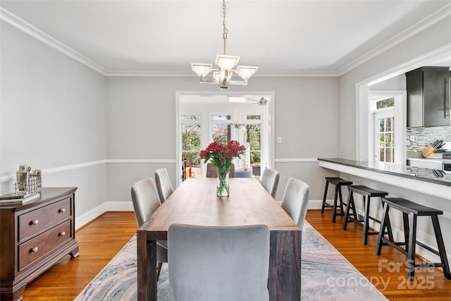 dining space featuring a wealth of natural light, crown molding, baseboards, and wood finished floors