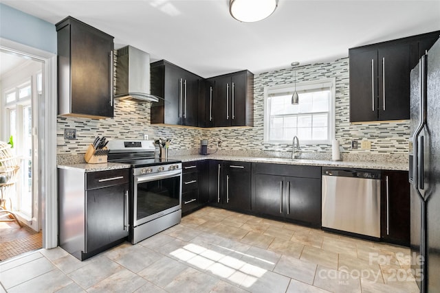 kitchen with backsplash, appliances with stainless steel finishes, a sink, dark cabinets, and wall chimney exhaust hood