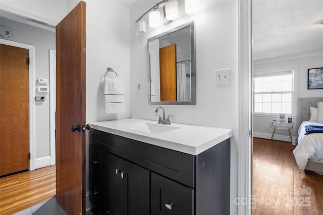 bathroom featuring baseboards, ensuite bath, ornamental molding, wood finished floors, and vanity