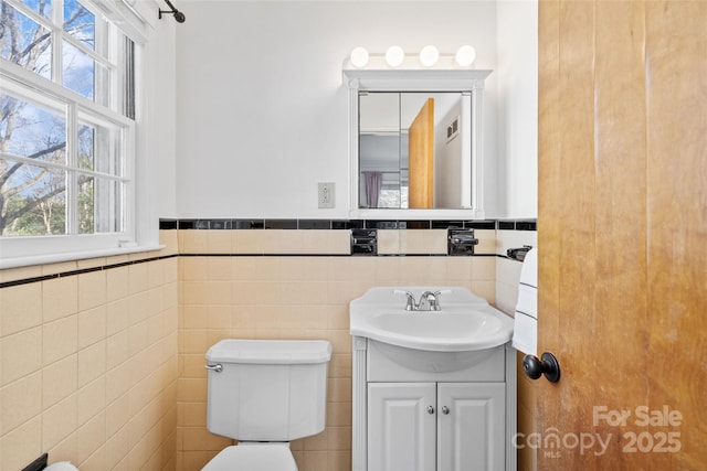 bathroom featuring toilet, wainscoting, tile walls, and vanity