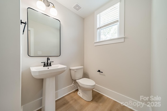 bathroom featuring visible vents, toilet, wood finished floors, a sink, and baseboards