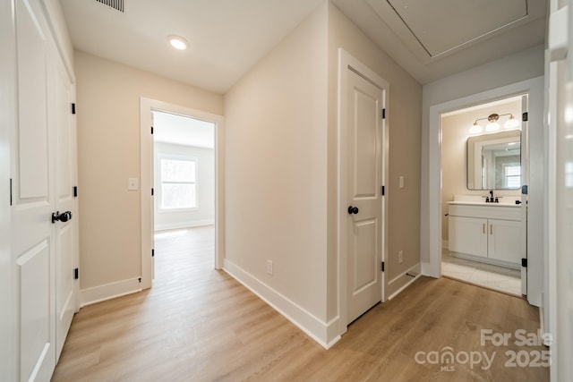 hall featuring light wood-type flooring, attic access, baseboards, and a sink