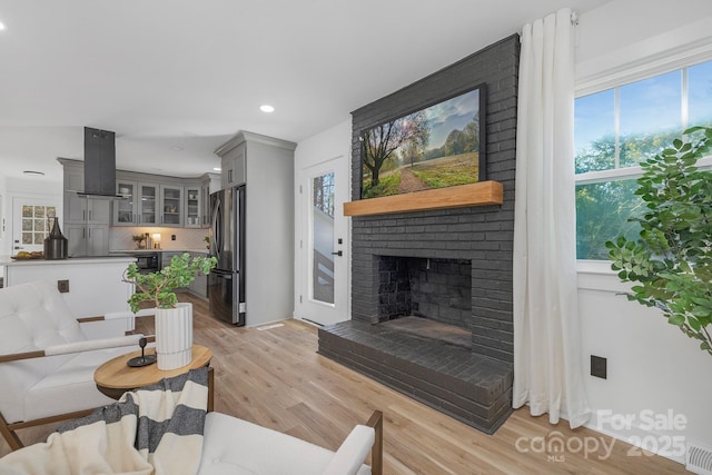 living area featuring light wood-style floors, recessed lighting, a brick fireplace, and visible vents