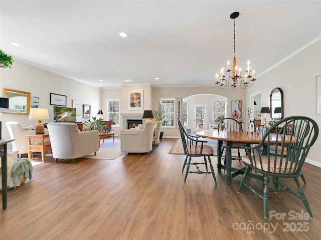 dining space with baseboards, wood finished floors, a lit fireplace, crown molding, and recessed lighting