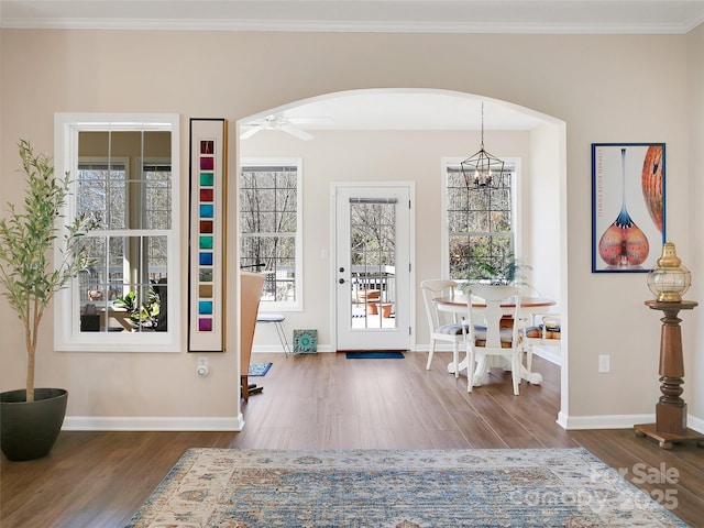 entryway with arched walkways, baseboards, wood finished floors, and crown molding