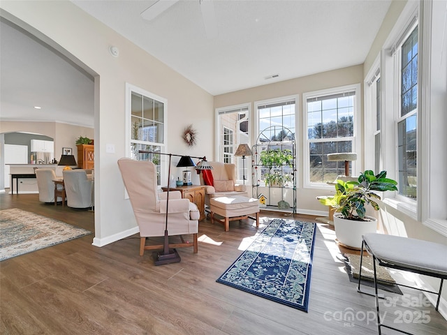 sitting room featuring arched walkways, wood finished floors, a ceiling fan, visible vents, and baseboards