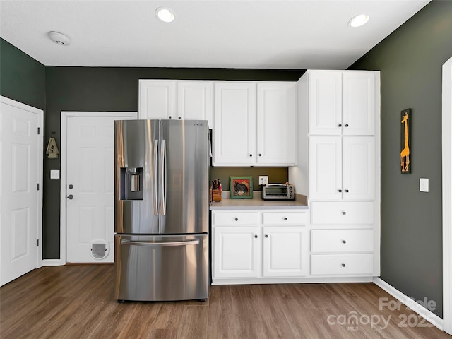 kitchen with baseboards, white cabinets, wood finished floors, light countertops, and stainless steel refrigerator with ice dispenser