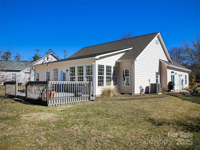 rear view of house featuring central air condition unit, a shingled roof, and a yard