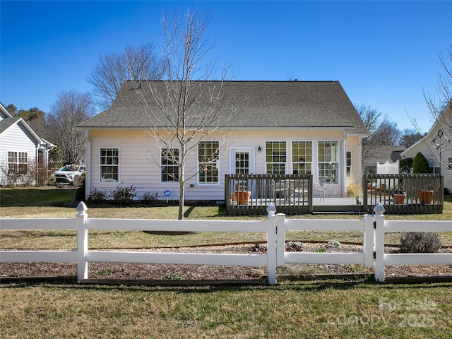 rear view of house featuring a fenced front yard, roof with shingles, a wooden deck, and a yard