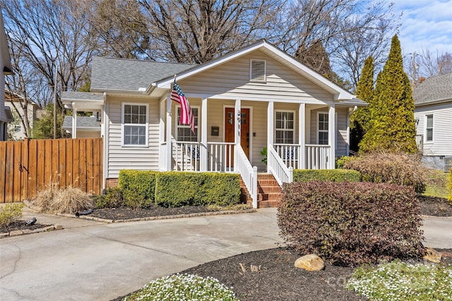 bungalow-style home featuring covered porch, roof with shingles, and fence