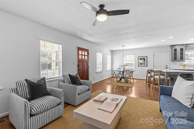 living room featuring ceiling fan, light wood finished floors, visible vents, and baseboards