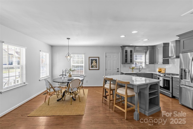 kitchen featuring dark wood finished floors, appliances with stainless steel finishes, gray cabinets, wall chimney range hood, and a sink