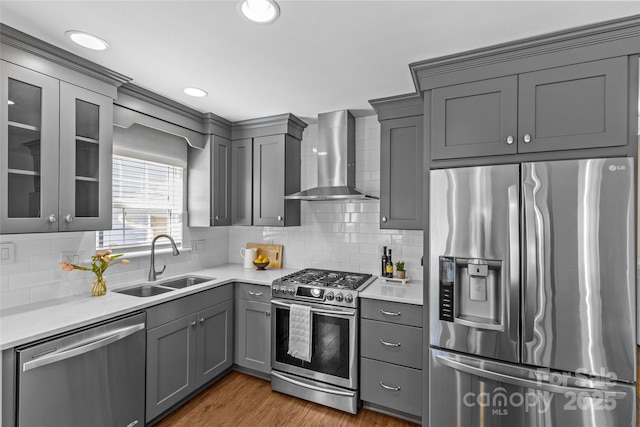 kitchen featuring appliances with stainless steel finishes, gray cabinets, light countertops, wall chimney range hood, and a sink