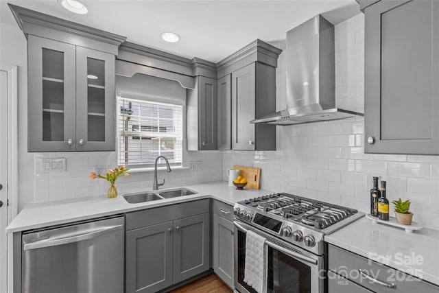 kitchen with wall chimney exhaust hood, glass insert cabinets, appliances with stainless steel finishes, gray cabinets, and a sink