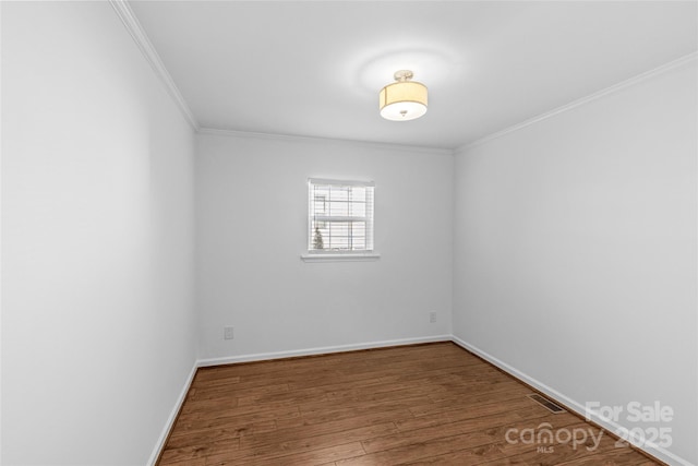 spare room featuring baseboards, wood finished floors, visible vents, and crown molding