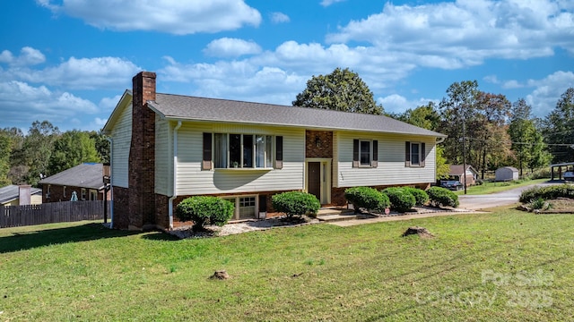 raised ranch with brick siding, a chimney, fence, and a front yard