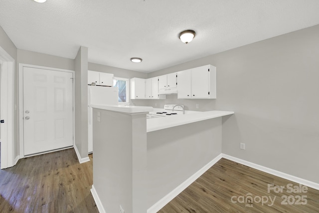 kitchen with under cabinet range hood, a peninsula, white cabinetry, light countertops, and range