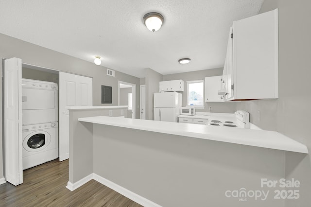 kitchen with stacked washer and clothes dryer, light countertops, white cabinetry, white appliances, and a peninsula