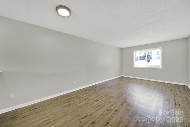 unfurnished room featuring a textured ceiling, baseboards, and wood finished floors