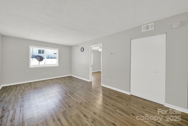 spare room with baseboards, a textured ceiling, visible vents, and wood finished floors