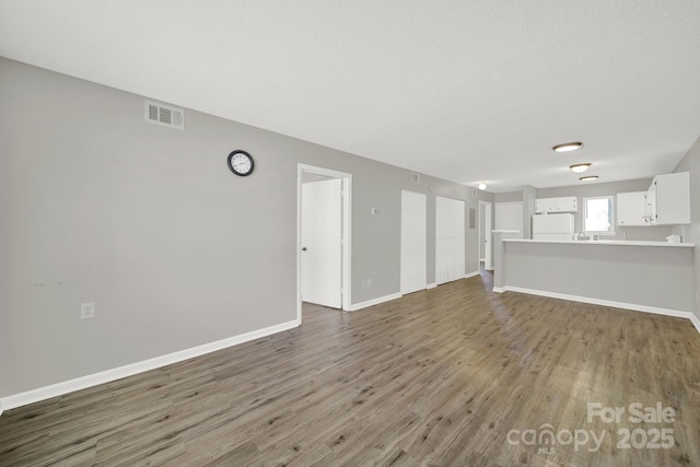 unfurnished living room with a textured ceiling, wood finished floors, visible vents, and baseboards