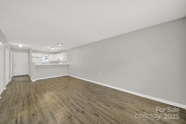 unfurnished living room featuring a textured ceiling, dark wood-style flooring, and baseboards