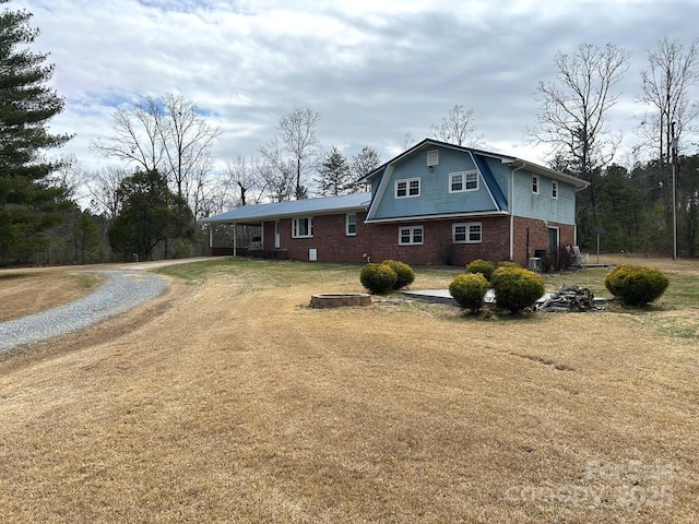 view of side of property with a yard, brick siding, driveway, and a gambrel roof