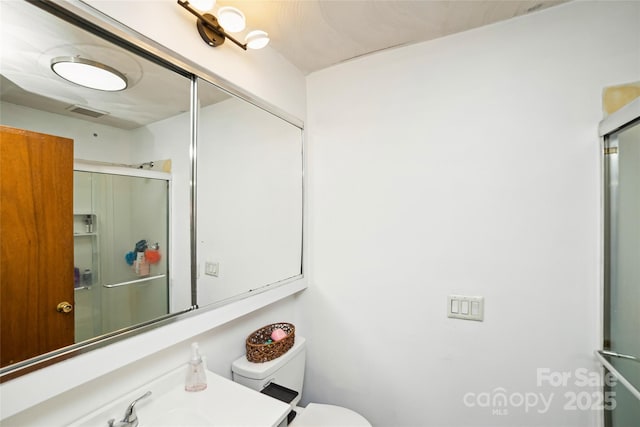 full bathroom featuring toilet, a shower with door, visible vents, and vanity