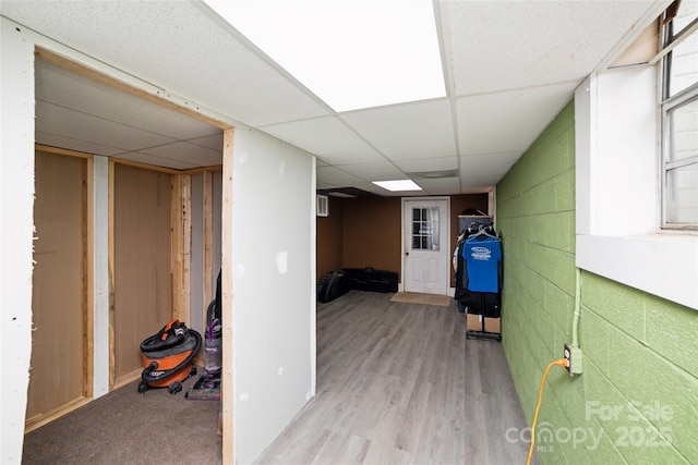 finished basement with concrete block wall, light wood finished floors, and a drop ceiling