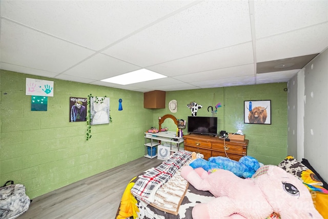 bedroom featuring concrete block wall, a drop ceiling, and wood finished floors