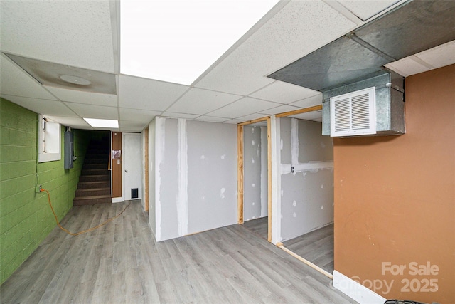 finished basement featuring stairs, a paneled ceiling, visible vents, and wood finished floors