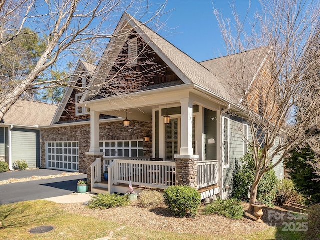 view of front facade with a garage, covered porch, driveway, and stone siding