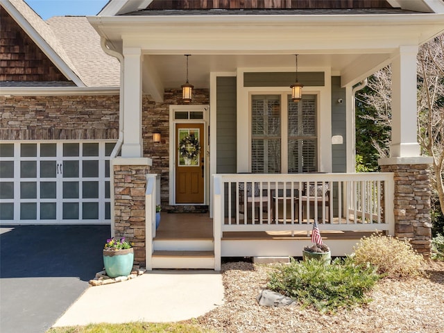 entrance to property featuring stone siding, a porch, an attached garage, and driveway