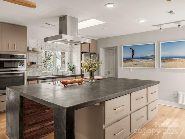 kitchen featuring tasteful backsplash, dark countertops, visible vents, a sink, and island range hood