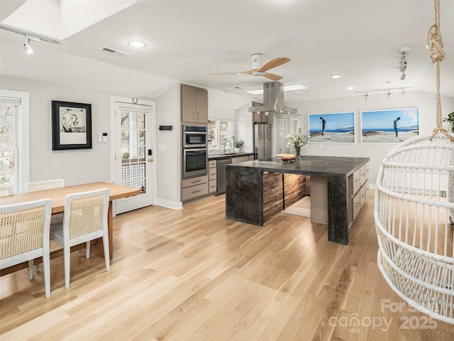 kitchen with visible vents, island range hood, dark countertops, appliances with stainless steel finishes, and a sink