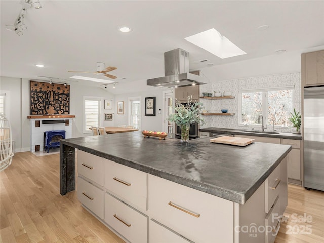 kitchen with island range hood, a sink, stainless steel built in fridge, light wood finished floors, and dark countertops