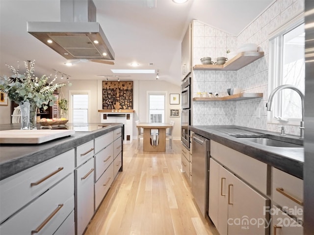 kitchen featuring island exhaust hood, dark countertops, light wood-style flooring, backsplash, and a sink