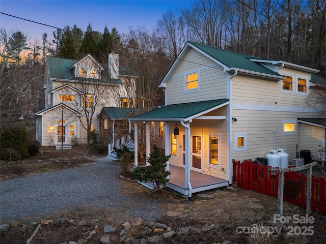 back of house at dusk featuring metal roof, fence, and a porch