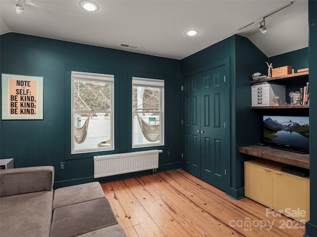 interior space with visible vents, radiator, lofted ceiling, rail lighting, and light wood-style floors