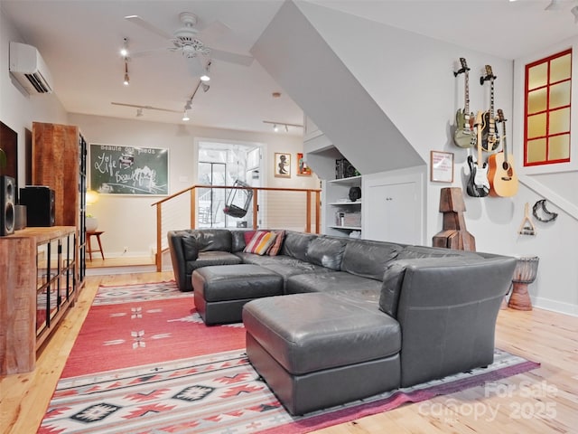 living area featuring an AC wall unit, wood finished floors, a ceiling fan, and baseboards