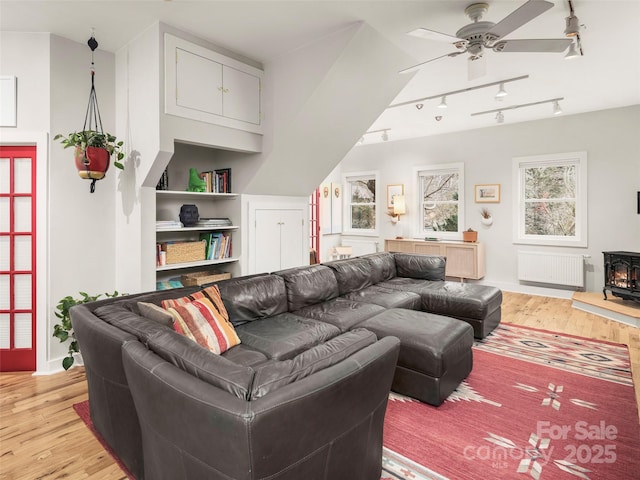 living area featuring light wood-style flooring, radiator heating unit, a ceiling fan, a wood stove, and baseboards