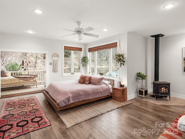 bedroom with recessed lighting, a wood stove, wood finished floors, access to outside, and baseboards