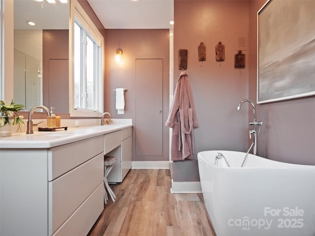 bathroom featuring double vanity, a freestanding bath, a sink, wood finished floors, and walk in shower