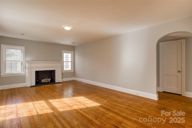 unfurnished living room featuring arched walkways, wood finished floors, and baseboards