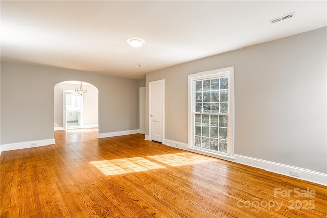 spare room with light wood-style floors, visible vents, arched walkways, and baseboards