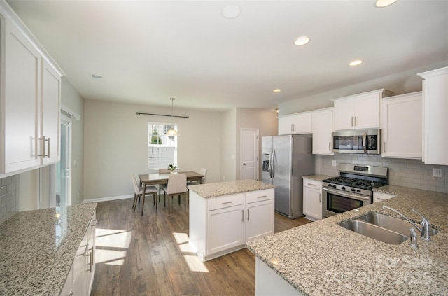 kitchen featuring dark wood-style floors, a kitchen island, a sink, appliances with stainless steel finishes, and tasteful backsplash