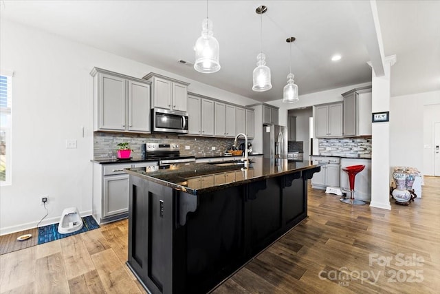 kitchen featuring stainless steel appliances, gray cabinetry, a sink, wood finished floors, and a kitchen bar